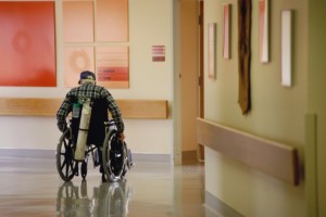 Man in wheelchair is neglected in a Nursing home hallway and sits alone.