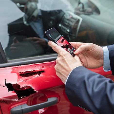 Hands of car insurance adjuster taking photo of car damage with phone