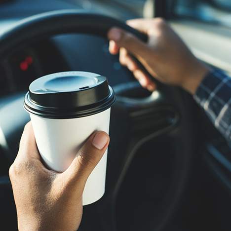 Hands holding coffee and steering wheel - understanding coffee intoxication while driving