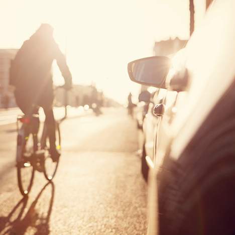 Cyclist riding in sunny street alongside cars, one of the dangers of motorcycles and bikes