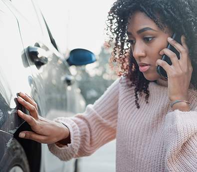 A woman on the phone while touching the side of a damaged car