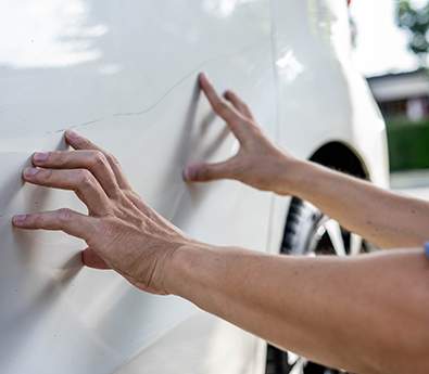 Two hands touching the side of a damaged car