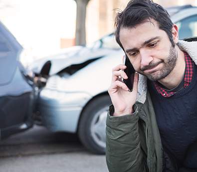 A man on the phone with a rear-ended car behind him