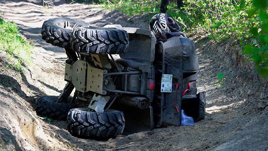 An ATV on its side after rolling over in an accident on a muddy trail and uneven ground