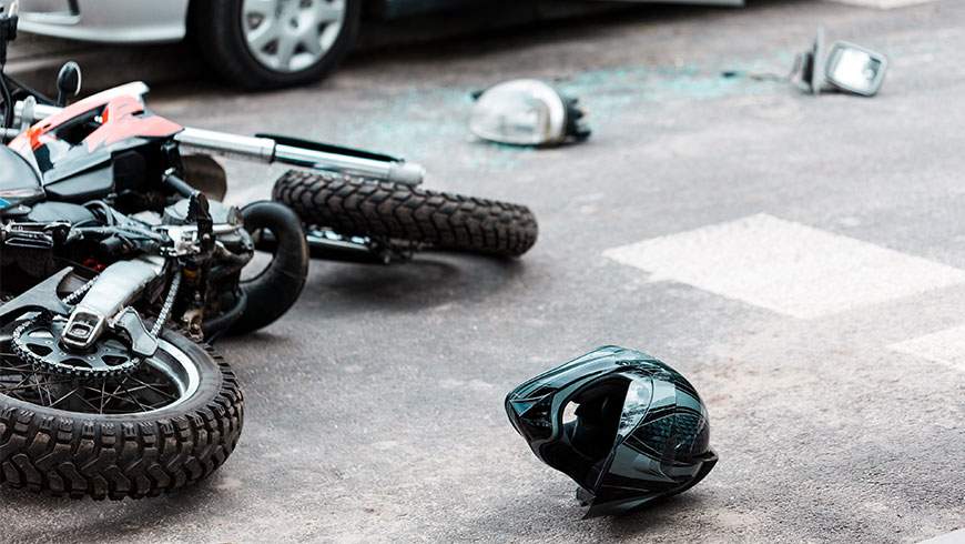 An overturned motorcycle and helmet lie on the street after a collision with a car