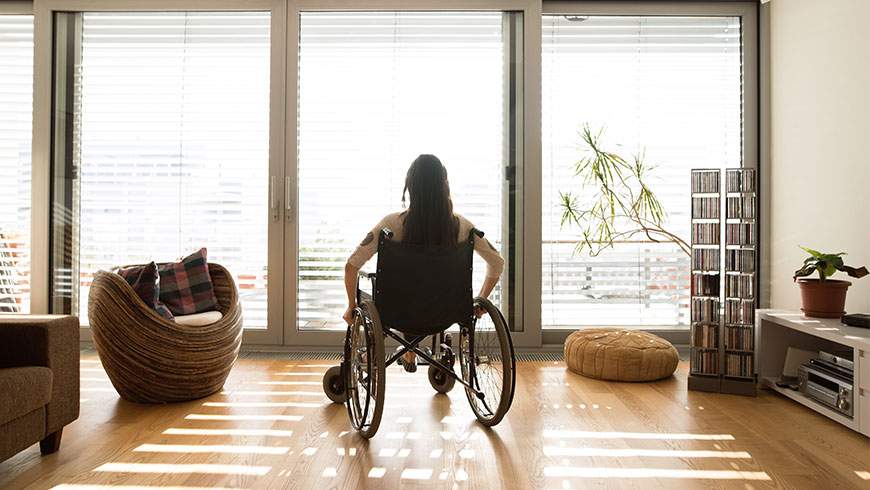 A young woman sits at home in a wheelchair after a traumatic spinal cord injury