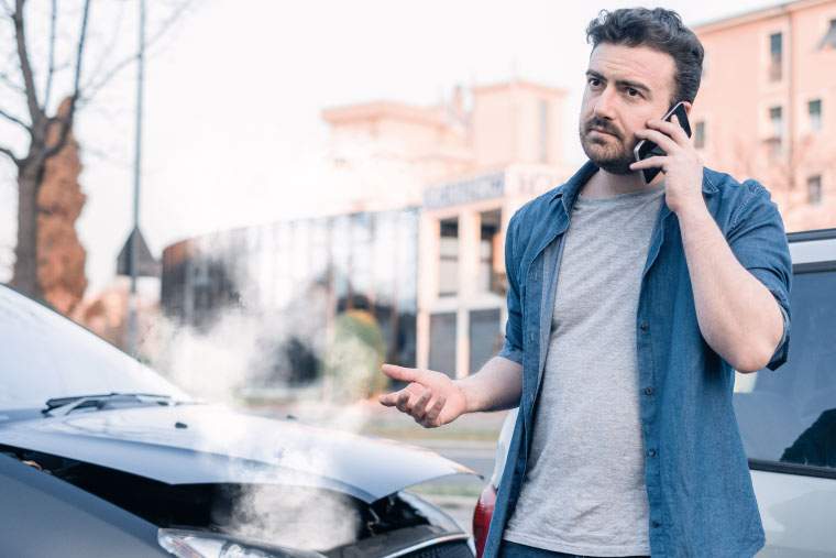 A man on the phone in front of a damaged car