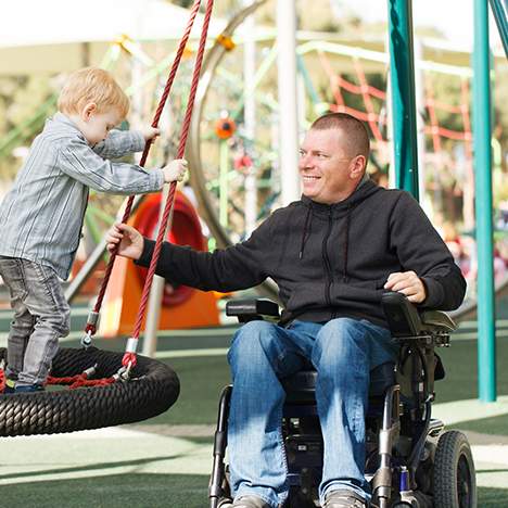 Man in a wheelchair playing with young children at a playground outside
