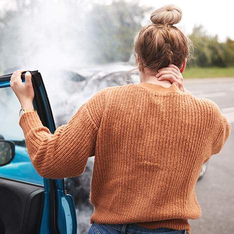 Woman holding her neck in front of car crash - know what to expect physically after a car accident
