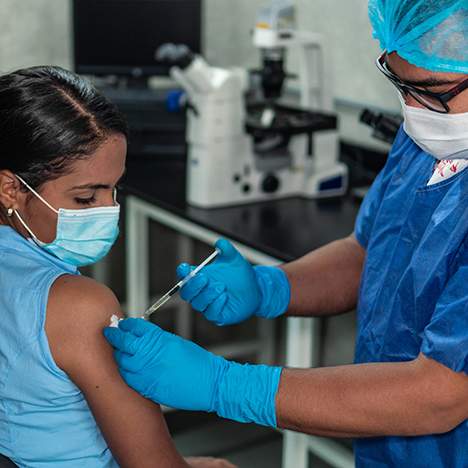 Woman in mask receiving shot, begging the question: can your employer require a COVID vaccine?