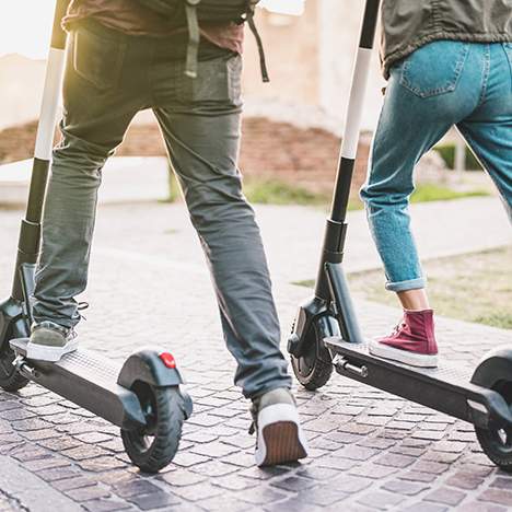 Two people riding e-scooters on brick-like surface - are electric scooters safe?