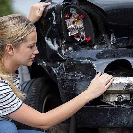 Woman examining car accident damage - find the best Riverside traffic accidents lawyer