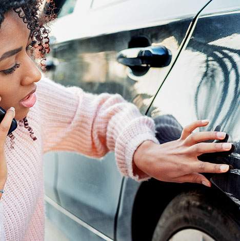 Woman on phone examining fender-bender damage - should I get a lawyer for a minor car accident?