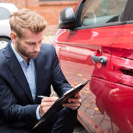 Man in suit with clipboard examining car damage - what happens if you wreck a rental car?