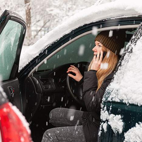 A woman on the phone with a car door open in a snow storm - learn the risks of winter car accidents