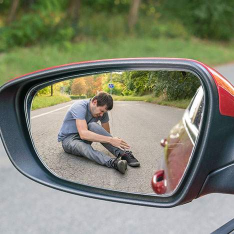 Man holding knee in view of a car mirror, suggesting the query: "Can I sue a hit and run driver?"