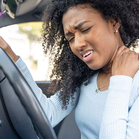 woman in car holding neck in visible pain - what are the most common injuries in a car accident