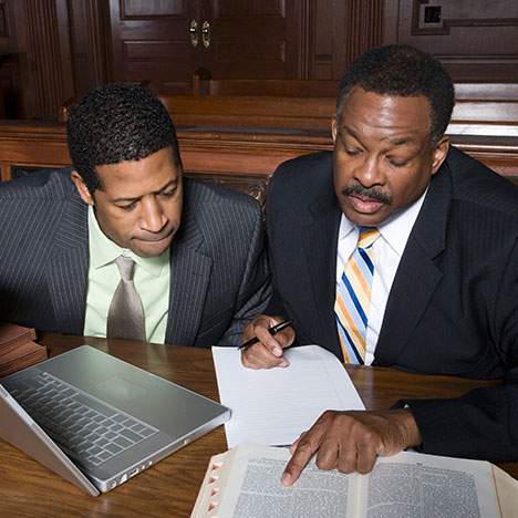 Two men looking at a laptop and books wondering how many personal injury cases go to trial