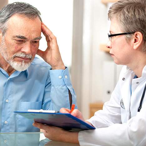 older man talking to a doctor holding a tablet asking can a car accident cause erectile dysfunction
