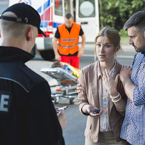 ar accident in another state scene with police officer and a man holding a women who is distraught