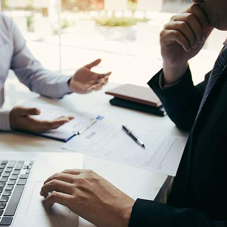 desk with laptop where two people are talking -Should you hire an attorney after a car accident